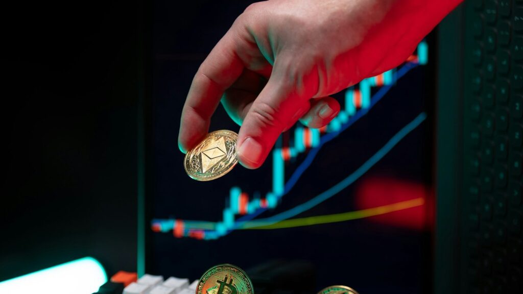يد تحمل عملة إيثيريوم ذهبية أمام شاشة تعرض مخططًا سعريًا صاعدًا