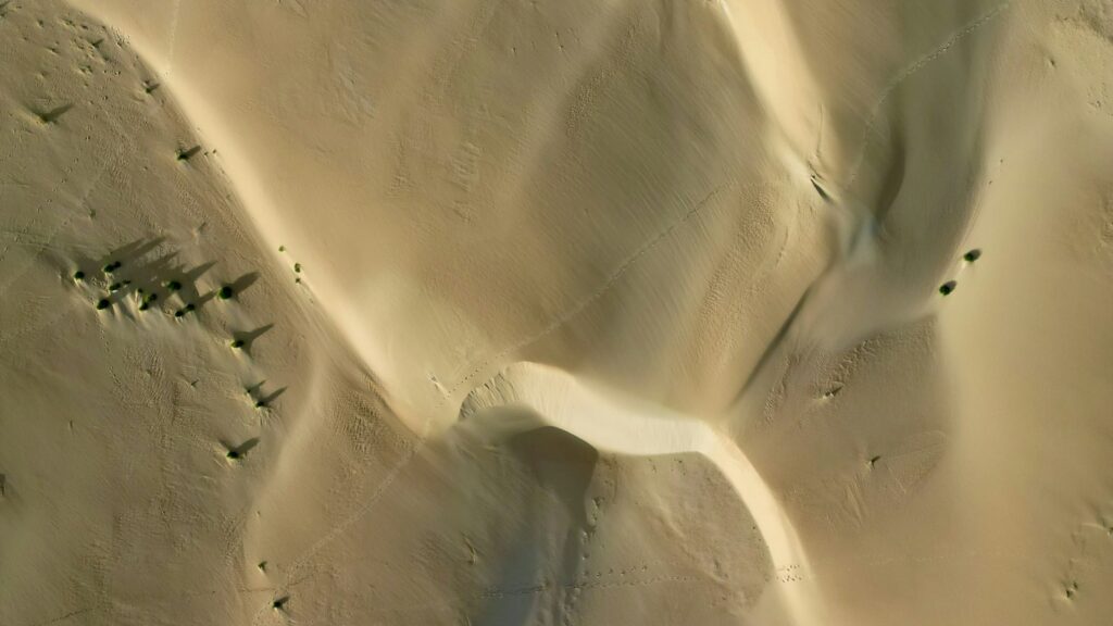 منظر جوي لكثبان رملية صحراوية بظلال طويلة عند غروب الشمس